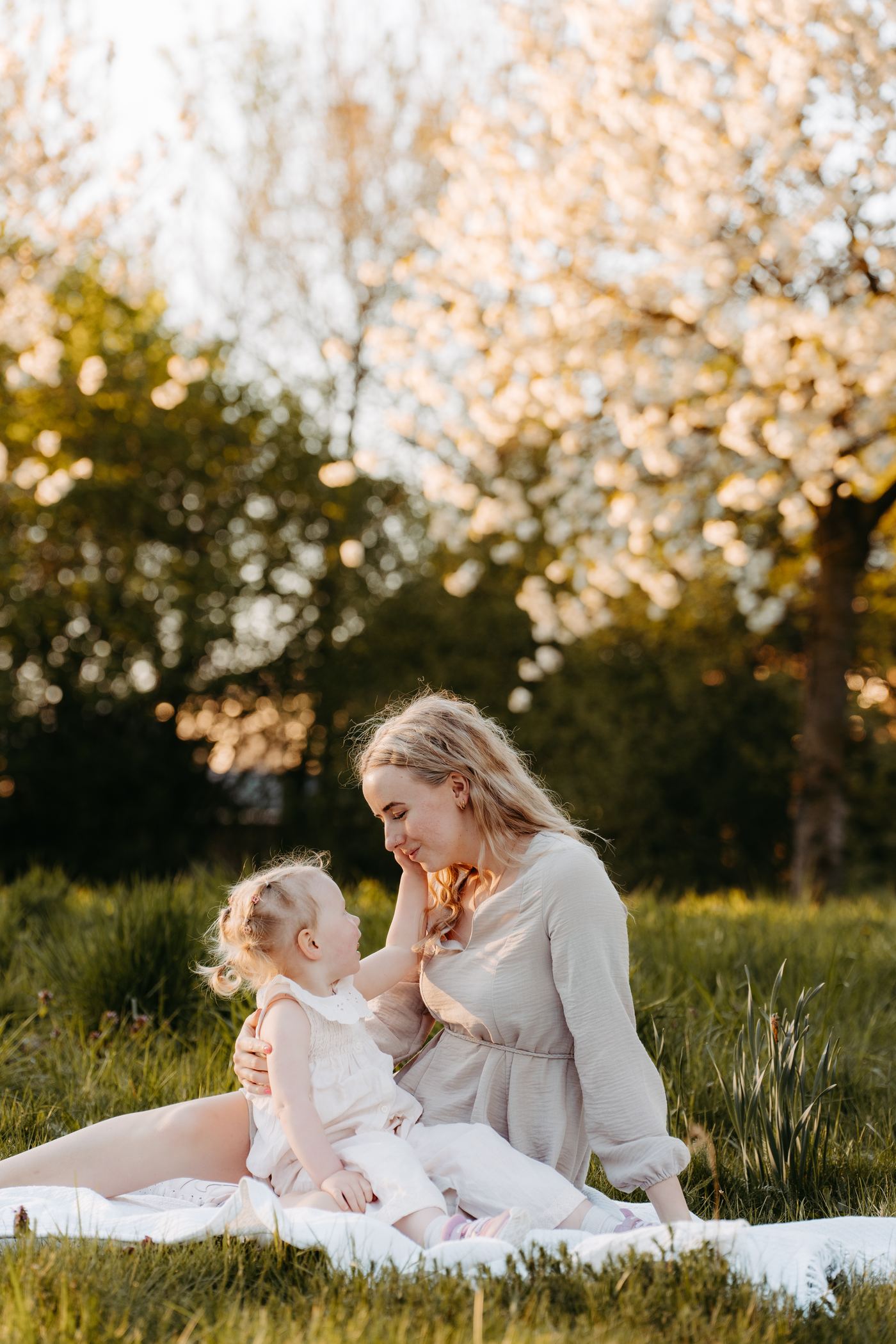 Familienfotografie Berlin – Zärtlicher Moment auf der Wiese unter blühenden Bäumen