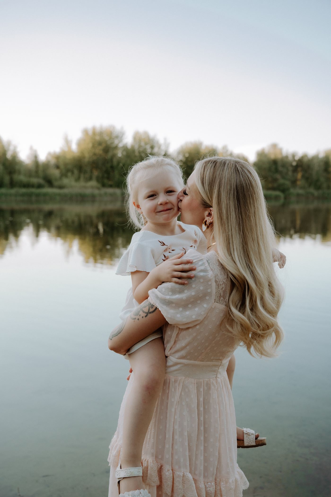 Familienfotograf Berlin – Mutter küsst Tochter am See im Abendlicht